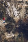Жінка з рюкзаком і гільзою стоїть на скелястому узбережжі озера у величних диких скелях — стокове фото