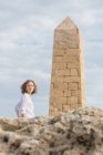 Молода ледача жінка дивиться на камеру біля кам'яної конструкції у вигляді вежі на камені — стокове фото