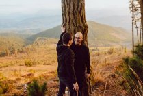 Весела гомосексуальна пара стоїть і дивиться один на одного біля дерева в горах — стокове фото