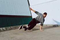 Guy performing handstand while dancing near wall of modern building — Stock Photo