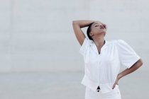 Модная коротковолосая этническая женщина в белой рубашке позирует на фоне серой стены — стоковое фото