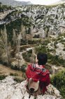 Vista posteriore di donna in viaggio con zaino seduto su alta scogliera rocciosa osservando bella valle — Foto stock