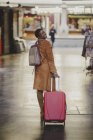 Smiling African American elegant woman with baggage walking on street near small shops — Stock Photo