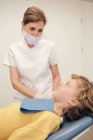 Mujer en uniforme médico hablando con un pequeño paciente en el consultorio del dentista - foto de stock