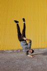 Молодий хлопець виконує тумбу під час танців біля стіни сучасної будівлі на міській вулиці — стокове фото