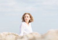 Молодая заботливая женщина сидит на берегу моря и смотрит в сторону — стоковое фото