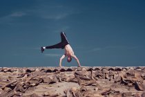 Young shirtless guy performing handstand on weathered roof of aged building against blue sky — Stock Photo