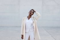 Mode kurzhaariges Model mit geschlossenen Augen im weißen Outfit posiert gegen graue Wand — Stockfoto
