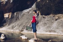 Woman standing on rock with case near clear water in lake — Stock Photo