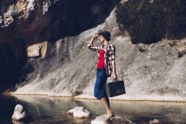 Mujer de pie sobre roca con el caso cerca de agua clara en el lago - foto de stock