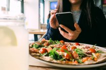 Cultivo femenino usando el teléfono móvil y sentado en la mesa con deliciosa ensalada en la cafetería - foto de stock