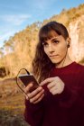 Young hipster woman with piercing and earphones listening music with mobile phone in countryside — Stock Photo