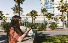 Chica adolescente mirando su teléfono inteligente en la calle en un día soleado - foto de stock