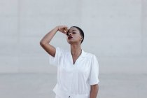 Чуттєва мода короткошерста етнічна жінка в білій сорочці позує на сіру стіну — стокове фото