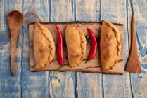 Empanadas horneadas caseras y chiles rojos frescos en tablero de madera - foto de stock