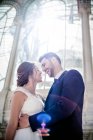Von unten umarmt ein junger eleganter Mann eine Frau im Hochzeitskleid in der Nähe des Retro-Palastes mit vielen Fenstern an sonnigen Tagen — Stockfoto
