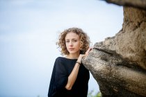 Молодая серьезная женщина опирается на скалу в природе и смотрит в камеру — стоковое фото