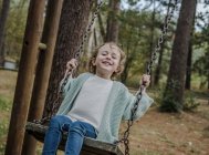 Позитивний щасливий дитина сидить на гойдалці між деревами в лісі — стокове фото