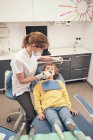 Жінка в масці і лікарська форма робить сканування зубів маленького хлопчика під час роботи в стоматологічній клініці — стокове фото