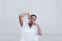 Мода короткошерста етнічна жінка в білій сорочці позує на сіру стіну — стокове фото