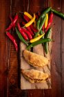 Rissóis cozidos em casa e pimentas verdes e vermelhas frescas a bordo em mesa de madeira marrom — Fotografia de Stock