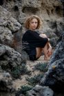 Jeune femme réfléchie assise dans des rochers et embrassant les genoux — Photo de stock