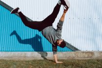 Attractive guy performing handstand and looking at camera while dancing near wall of modern building on city street — Stock Photo