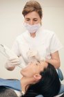 Woman in gloves and mask using modern equipment for scan of teeth of female patient in dentist office — Stock Photo