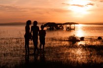 Back view of silhouettes of kids standing on shore near water and laundry in evening in Ometepe, Nicaragua — Stock Photo