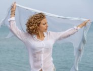 Junge Frau hält Schal in erhobenen Händen gegen Meerwasseroberfläche — Stockfoto