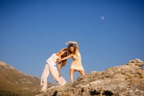 Jovens mulheres misteriosas com as mãos erguidas posando em rochas perto da colina e céu azul com lua — Fotografia de Stock