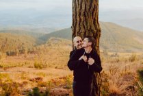 Весела Гомосексуальна пара, що охоплює біля дерева в лісі і мальовничий вид на долину — стокове фото