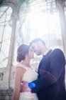From below young elegant man embracing woman in wedding dress near retro palace with many windows in sunny day — Stock Photo
