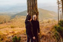 Весела гомосексуальна пара обіймає біля дерева в лісі і мальовничий вид на долину — стокове фото