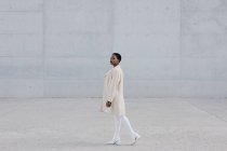 Мода короткошерста етнічна жінка в білому вбранні, що йде перед сірою стіною — стокове фото