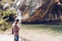 Вид збоку подорожуючого чоловіка, який стоїть на піщаному березі тихого озера проти скелі — стокове фото