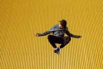 Guapo barbudo en traje de moda saltando contra la pared amarilla del edificio moderno - foto de stock