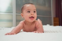 Смешной маленький голый новорожденный смотрит в сторону и лежит на кровати в комнате — стоковое фото