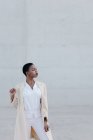 Мода короткошерста етнічна жінка в білому вбранні позує на сіру стіну — стокове фото