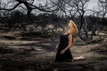 Молодая балерина в черной одежде танцует на земле между сухим лесом — стоковое фото