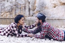 Side view of young couple lying on rock coast of mountain river near cliff — Stock Photo
