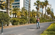 Junge Frau mit Sonnenbrille spaziert auf sonnigem Boulevard vor Palmen — Stockfoto