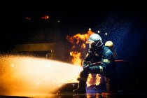 Homem irreconhecível em uniforme de bombeiro suprimindo fogo com fluxo pesado de água — Fotografia de Stock