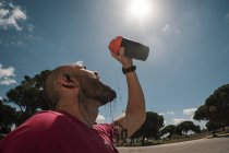 Homme buvant pendant l'entraînement contre le ciel bleu avec des nuages — Photo de stock