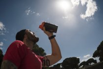 Mann trinkt beim Training vor blauem Himmel mit Wolken — Stockfoto