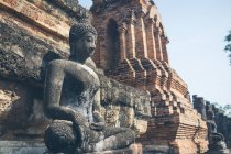 Estatua envejecida de Buddha situada cerca de las paredes de piedra maltrecho del templo oriental antiguo en Tailandia - foto de stock