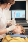 Mulher em máscara e uniforme médico fazendo varredura de dentes de menino enquanto trabalhava na clínica odontológica — Fotografia de Stock