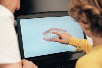Female dentist demonstrating teeth scan on laptop screen to little boy in modern clinic — Stock Photo