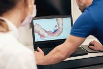 Анонімний чоловік демонструє сканування зубів на екрані ноутбука до невпізнаваної жінки-стоматолога в сучасній клініці — стокове фото