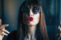 Atractiva hembra con labios rojos besando con pasión el vidrio transparente limpio - foto de stock